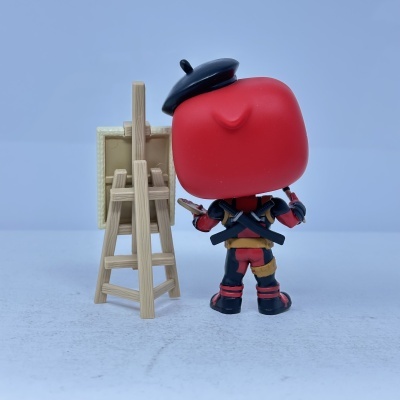 Boneco Deadpool com boina preta pintando em cavalete de madeira