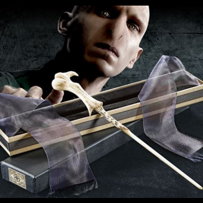 Varinha mágica creme numa caixa de madeira com tecidos roxos, fundo escuro e cabeça de personagem visível.