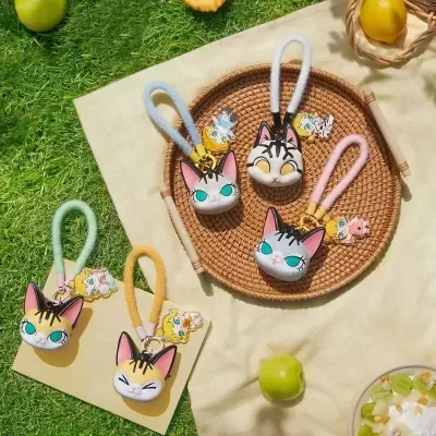Porta-chaves com pendentes de gato em várias cores e expressões com argolas coloridas em tecido e pendentes de personagens animados sobre bandeja e tecido no relvado