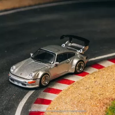 Miniatura de carro desportivo prateado com spoiler preto e rodas douradas num circuito de corrida