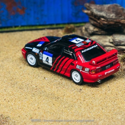 Carro de rally em miniatura vermelho e preto com decoração num cenário arenoso