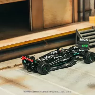 Miniatura de carro de Fórmula 1 preto com várias marcas em ambiente de garagem simulado