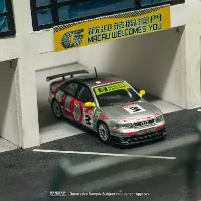 Miniatura de carro de corrida Audi A4 cinzento num box de pista com sinais Macau Welcomes You e Grand Prix.