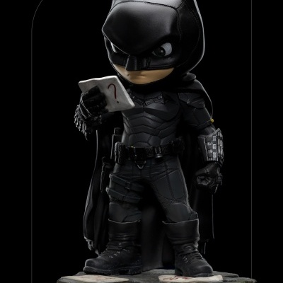 Figurino colecionável do Batman com roupa preta e capa, segurando cartão com ponto de interrogação
