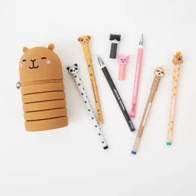Estojo castanho em formato de urso e canetas decorativas de animais sobre fundo branco.