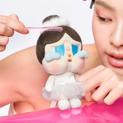 Boneca de pelúcia com saia de tule branco e pente rosa a pentear o cabelo