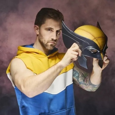 Homem a segurar máscara de Wolverine preta e amarela com fundo roxo.