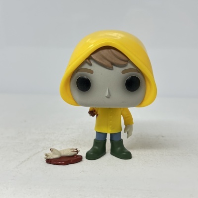 Figura de brinquedo de vinil com capa amarela e braço cortado no chão