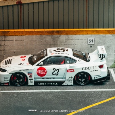 Miniatura de carro de corrida branco com número 23 e várias marcas ao lado de parede cinza com faixa amarela