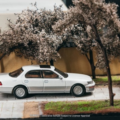 Miniatura de carro branco num cenário miniatura com árvores em flor e passeio pavimentado
