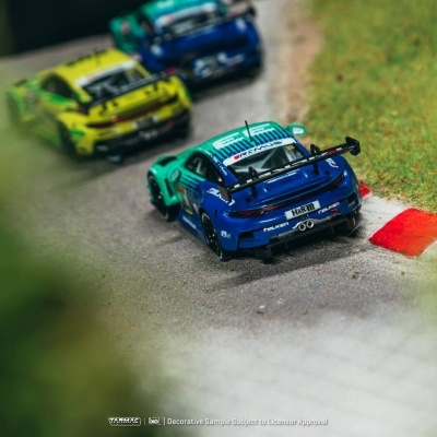 Modelo de carrinho de corrida azul a seguir carrinhos amarelo e azul numa pista de corrida com relva.
