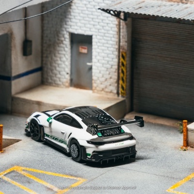 Miniatura de carro desportivo branco GT3 RS num cenário industrial com paredes de tijolo branco e porta cinza.
