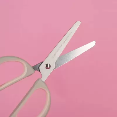 Tesoura de aço inoxidável com punho bege claro em fundo rosa