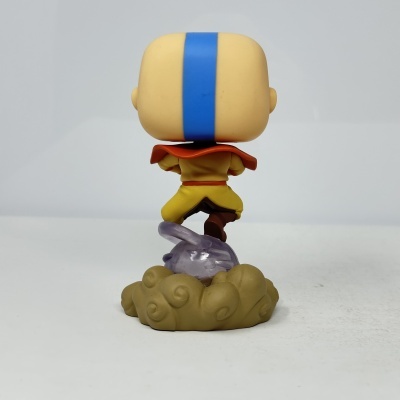 Figura colecionável de personagem com roupa amarela e listra azul na cabeça sentada em nuvem castanha com base translúcida roxa.