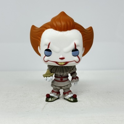 Boneco colecionável com rosto de palhaço e cabelo castanho-avermelhado segurando barco de papel.