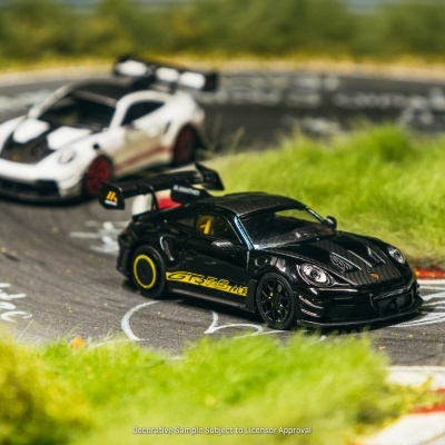 Dois carros de corrida em miniatura preto e branco numa pista de corrida em miniatura com grama ao redor