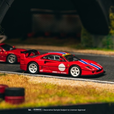 Miniatura de carro desportivo vermelho de corrida numa pista com vedação metálica e vegetação