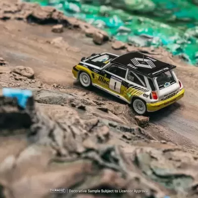 Miniatura de carro de rally Renault preto, branco e amarelo com terreno acidentado ao fundo
