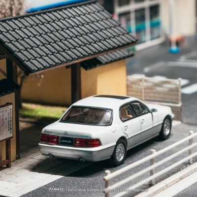 Modelo em miniatura de carro branco estacionado junto a parada de autocarro em madeira com telhado preto