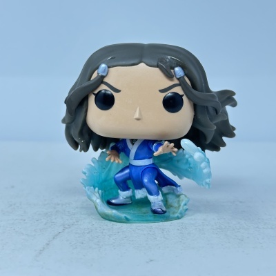 Figura de vinil estilo Funko Pop com cabelo castanho escuro e roupa azul rodeada por efeito de água.