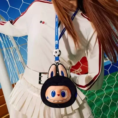 Bolsa divertida pendurada com cordão azul com bola de futebol, usada com roupa branca e riscas vermelhas junto a baliza de futebol
