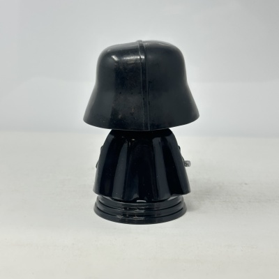 Figura de ação preta vista de costas com capacete arredondado e capa.