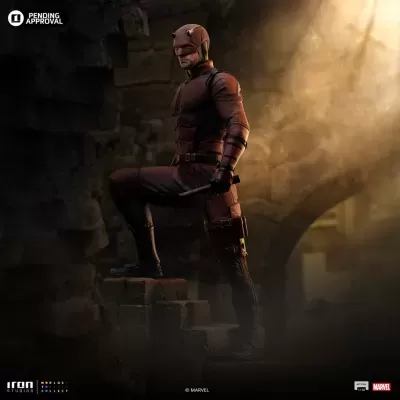 Estátua do Daredevil na posição de pé num degrau de pedra com bastão e fato vermelho.