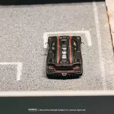 Miniatura de carro desportivo preto com detalhes em vermelho estacionado num parque de estacionamento.