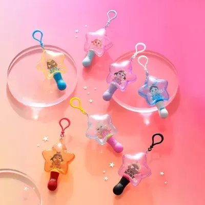 Conjunto de porta-chaves coloridos em forma de estrela com chupetas, sobre fundo rosa e objetos redondos transparentes.