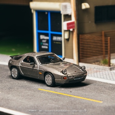 Miniatura de carro desportivo metálico sobre estrada com edifícios ao fundo