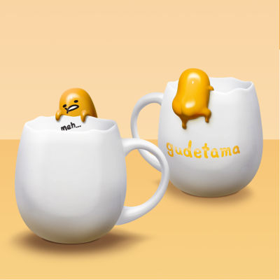 Duas canecas brancas de ovo partido com figuras amarelas animadas de ovos e texto 'gudetama' e 'meh...'