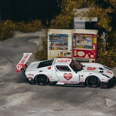 Miniatura de carro de corrida branco com texto vermelho e coração numa estrada em miniatura com máquinas de venda automática.
