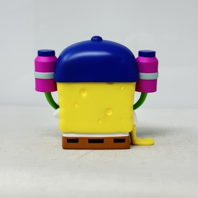 Figura de plástico amarela com chapéu azul e mochilas rosas vista de costas