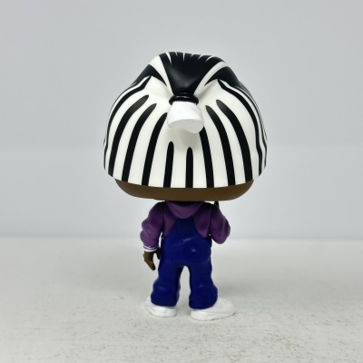 Boneco de vinil com cabelo preto e branco listrado, roupa roxa e azul, visto de costas.