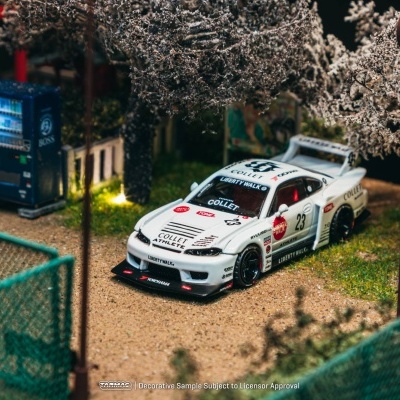 Miniatura de carro de corrida branco num cenário detalhado com árvores, cerca verde e máquina de venda automática