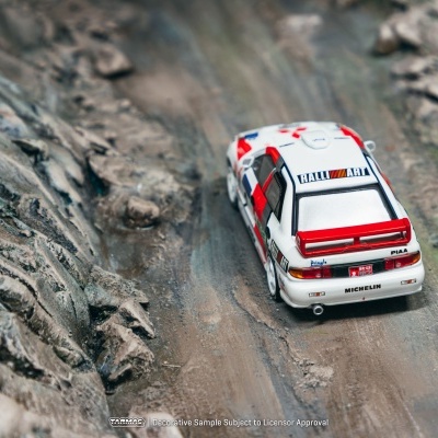 Miniatura de carro de rali branco com detalhes a vermelho e azul em terreno acidentado
