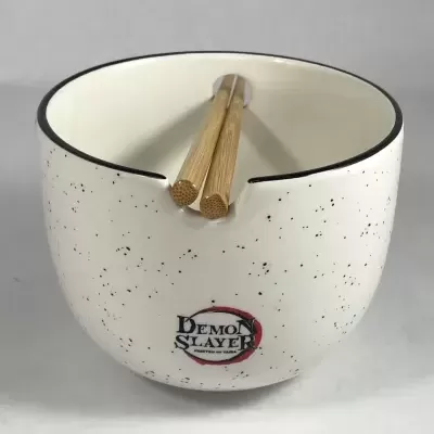 Tigela branca com pintas pretas e texto Demon Slayer com pauzinhos de madeira