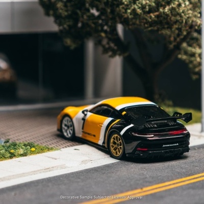 Miniatura de carro desportivo amarelo, branco e preto numa maquete de rua com árvores