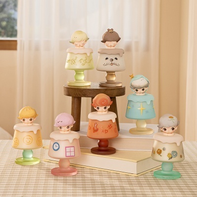 Sete mini candeeiros decorativos coloridos com personagens na parte superior, em cima de tecido xadrez e livros, em ambiente interior com cortinas.