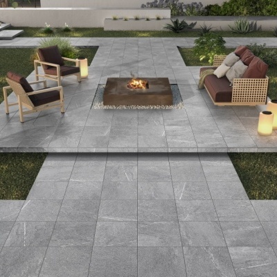 Espaço exterior com mobiliário de jardim em madeira, vime, almofadas e luminárias iluminadas.