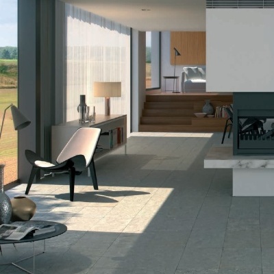 Sala moderna com cadeira preta, mesa redonda, candeeiro de mesa e lareira, chão em pedra cinzenta e janelas amplas