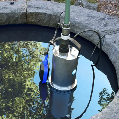 Bomba submersível metálica numa fonte com paredes de pedra cinzenta e cabos eléctricos.