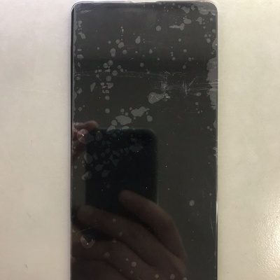 Smartphone com ecrã preto marcado por manchas e riscos sobre superfície clara