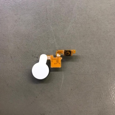 Peça eletrónica com circuito flexível laranja e componente circular branco sobre superfície cinzenta