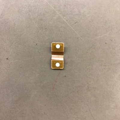 Peça metálica dourada com dois quadrados e pontos brancos sobre superfície cinza