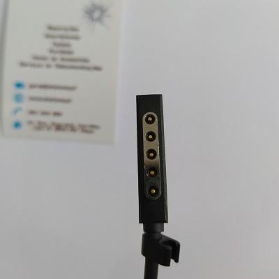 Cabo preto com conector magnético de cinco pinos dourados e cartão branco desfocado ao fundo