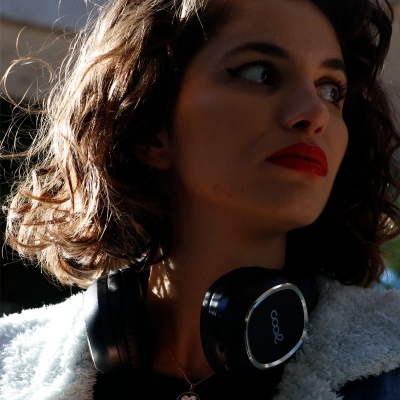 Mulher com auscultadores pretos Oppo e casaco branco peludo em luz natural