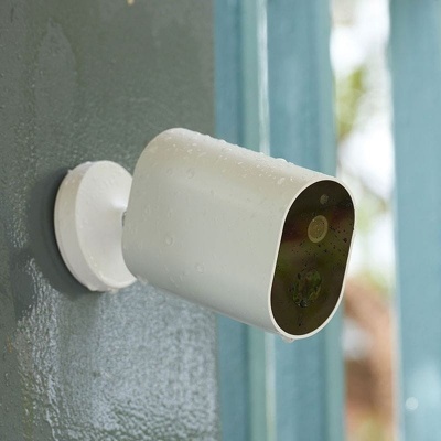 Câmara de vigilância branca com gotas de água fixada numa parede cinzenta junto a uma porta azul