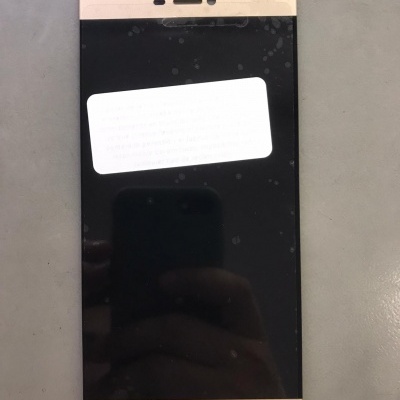 Smartphone com ecrã preto e bordas douradas com etiqueta branca numa superfície cinzenta