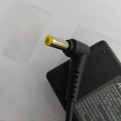 Adaptador de alimentação preto com conector de ponta amarela sobre papel